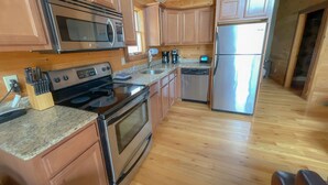 Une cuisine moderne avec des meubles en bois, des appareils en acier inoxydable, des plans de travail en granit et un plancher en bois.