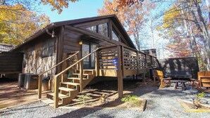 Une cabane avec une façade en bois, un escalier menant à une terrasse et des sièges à l’extérieur.