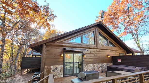 Une cabane avec des fondations en pierre, de grandes fenêtres et une terrasse dotée d’un barbecue.