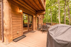 Relax on the covered deck with a grill, surrounded by lush greenery.
