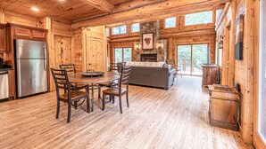 A log cabin interior with a dining area, kitchen, and fireplace. - Watershed 1 - Modern-Rustic, Luxury, One King Bedroom Cabin (Bryson City)
