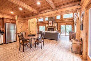 A log cabin interior with a dining area, kitchen, and fireplace.
