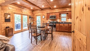 A wooden cabin interior with a dining area, kitchen, and large windows. - Watershed 1 - Modern-Rustic, Luxury, One King Bedroom Cabin (Bryson City)