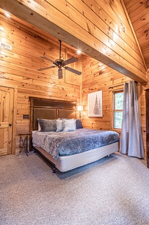 Relax in this inviting bedroom with a large bed and ceiling fan, surrounded by warm, cozy decor.
