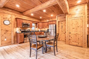 A wooden cabin interior with a kitchen featuring wooden cabinets, a stainless steel refrigerator, and a dining table with chairs.
