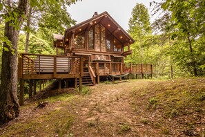 A wooden cabin with a deck, surrounded by trees.