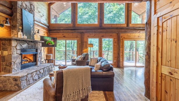 Ein großzügiges Holzblockhaus-Interieur mit Kamin aus Stein, einer Ledersofa und großen Fenstern mit Blick auf den umliegenden Wald.