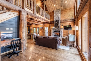 L’intérieur d’une cabane en rondins, avec une cheminée en pierre, des meubles en bois et un balcon.