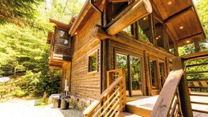 Eine Holzhütte mit einer Treppe, die zu einer Terrasse führt, umgeben von dichtem Wald.