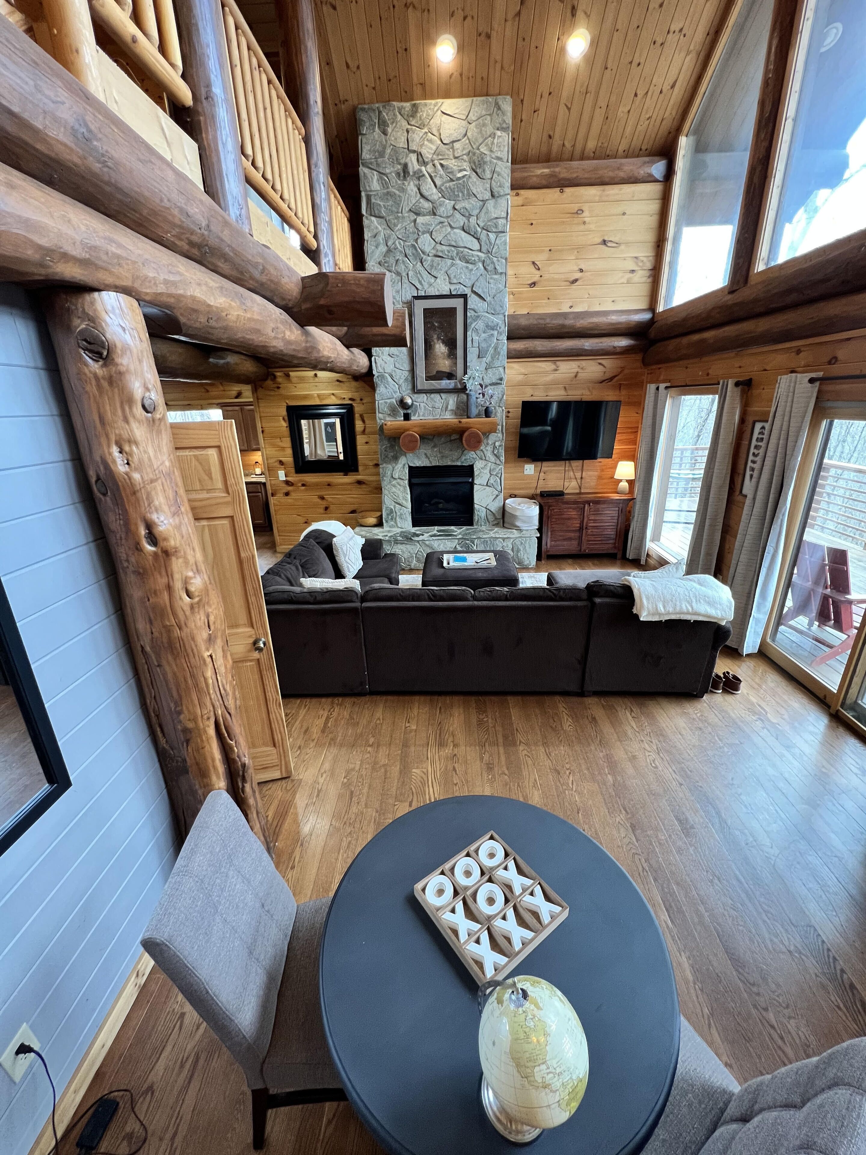 A cozy log cabin interior with a stone fireplace, a large sofa, and a round table with a globe.