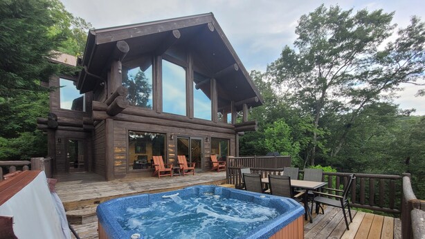 Una cabaña de madera con un jacuzzi en una terraza, rodeada de árboles.