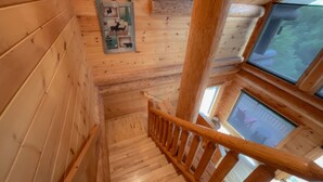 Una escalera de madera con barandilla, paredes de madera y una ventana que da a vistas de vegetación.