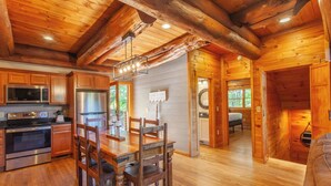 L’intérieur d’une cabane en rondins, avec une table à manger en bois, des chaises, une cuisine équipée d’appareils électroménagers modernes et une cheminée chaleureuse.