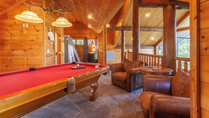 Une pièce chaleureuse avec une table de billard, des fauteuils en cuir et des murs en bois.