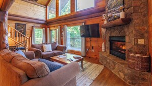 Un intérieur de chalet chaleureux avec une cheminée en pierre, des meubles en bois et de grandes fenêtres.