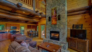 L’intérieur d’une cabane en rondins, avec une cheminée en pierre, des meubles en bois et un coin cuisine.
