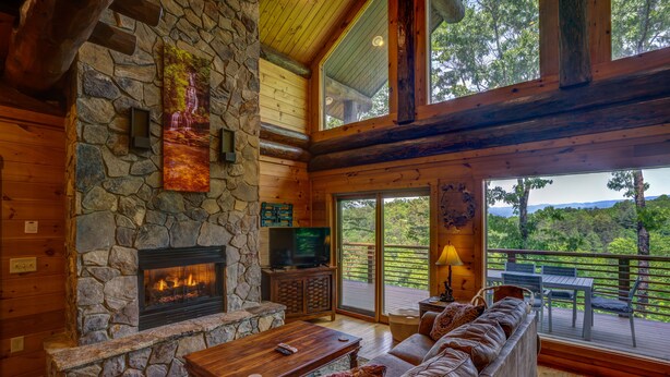 Un intérieur de chalet chaleureux avec une cheminée en pierre, des meubles en bois et un balcon offrant une vue panoramique.