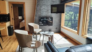 Una sala de estar acogedora con chimenea, televisor montado en la pared y un amplio ventanal con vistas al exterior.