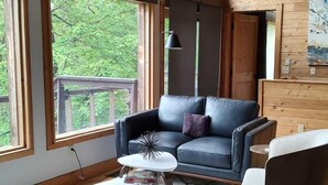 Un moderno salón con un sofá de cuero, una mesa de centro redonda y una silla. Amplias ventanas ofrecen vistas al exterior.