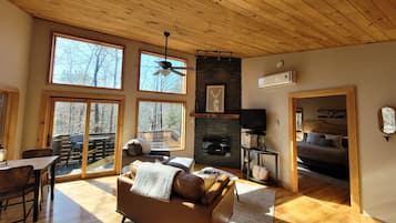 A spacious living area with a wooden ceiling, large windows, a fireplace, and a cozy seating area.