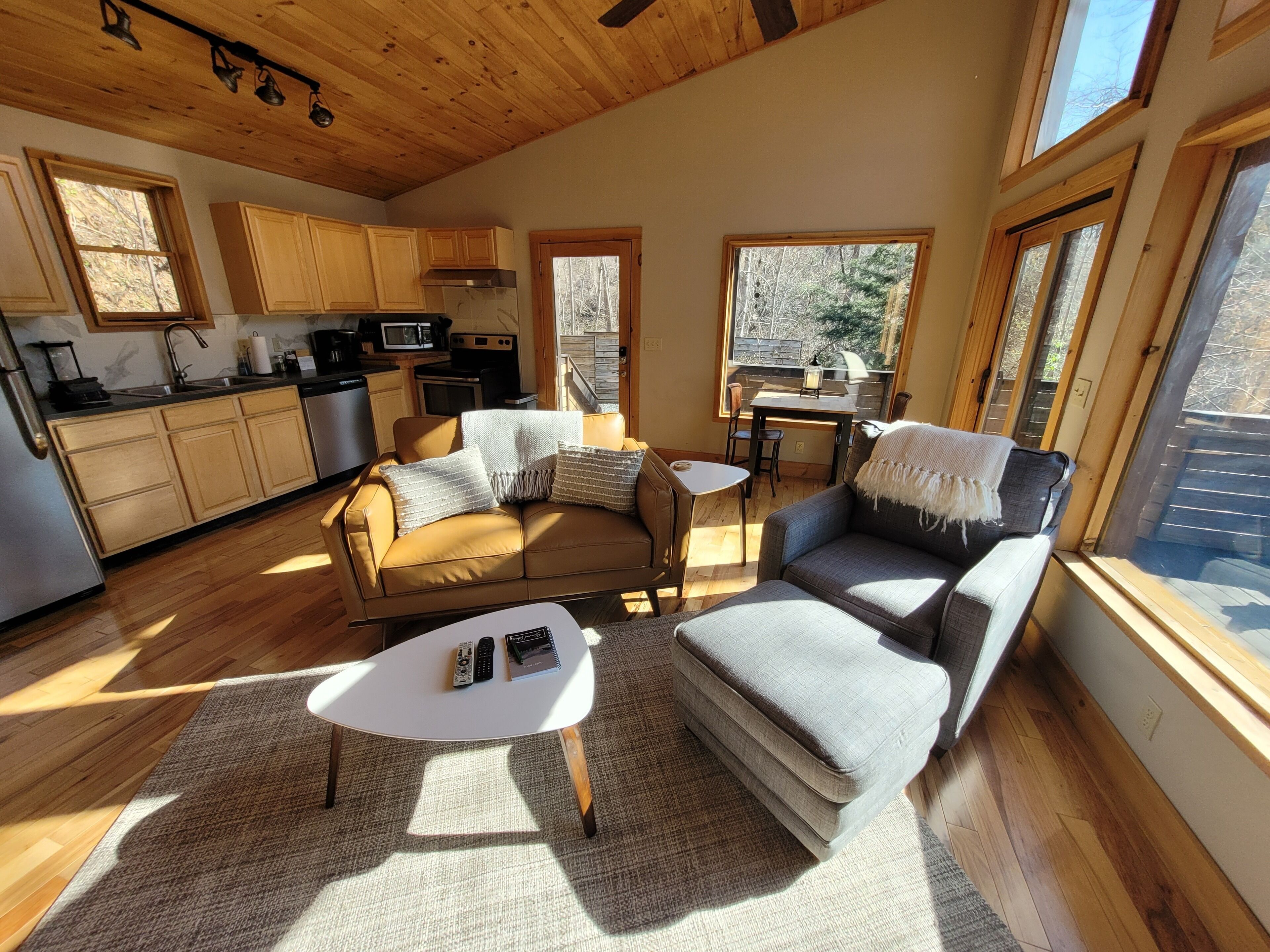 A cozy living area with a sofa, armchairs, and a coffee table. A kitchen with wooden cabinets and appliances is visible in the background.