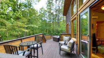 A wooden deck with outdoor furniture, surrounded by dense forest.