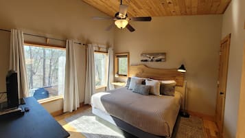 A bedroom with a bed, a desk, a ceiling fan, and windows with curtains.