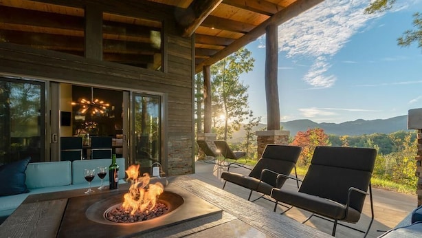 Un espacio al aire libre moderno con asientos, una chimenea, sillones cómodos y vistas a las montañas.