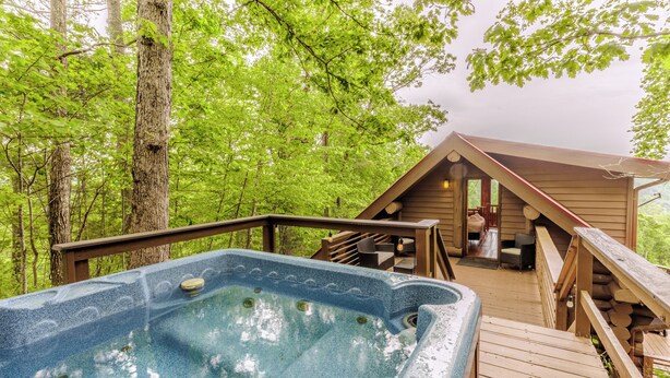 A hot tub on a wooden deck surrounded by trees, with a wooden cabin in the background. - Fontana View 1 - Ridgetop - Gated Community (Almond)