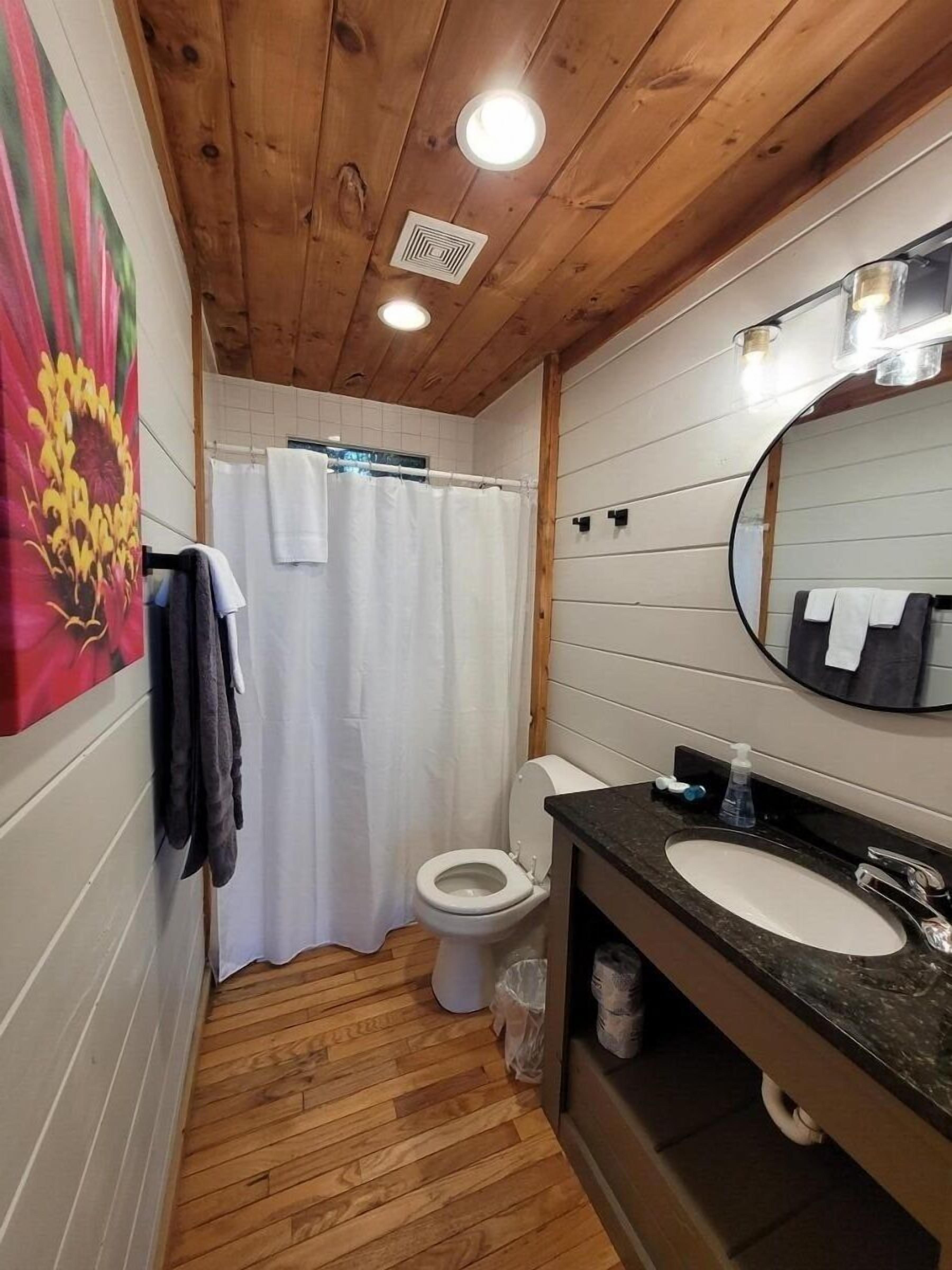 Un baño con paneles de madera, un inodoro blanco, una cortina de ducha, un lavabo con espejo y un perchero para toallas.
