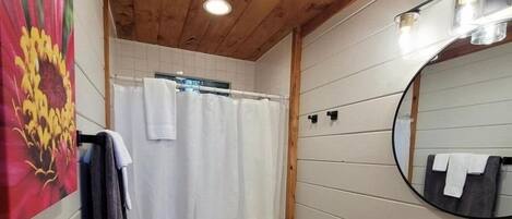 Un baño con paneles de madera, un inodoro blanco, una cortina de ducha, un lavabo con espejo y un perchero para toallas.