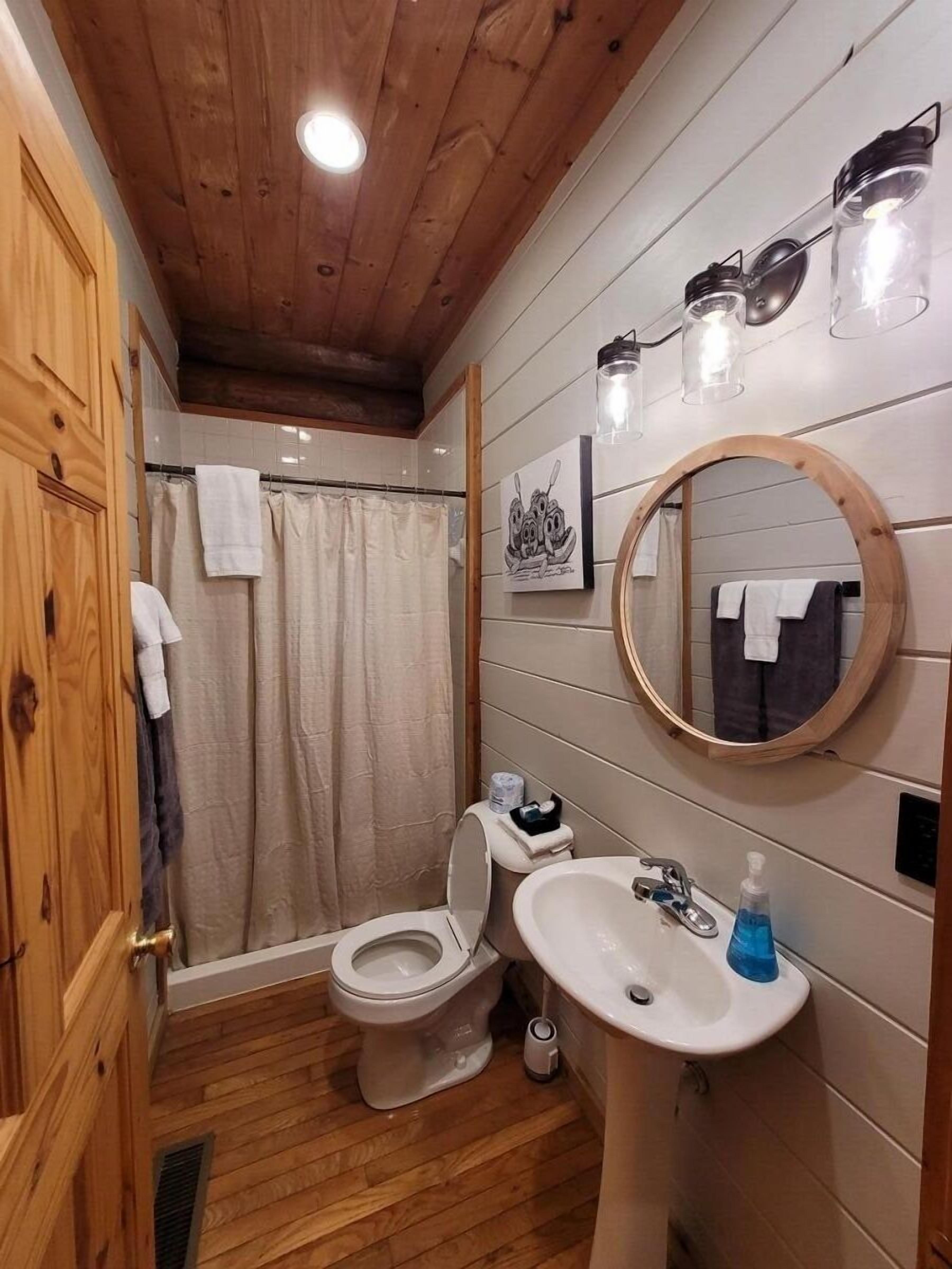 A wooden-paneled bathroom with a toilet, sink, and shower.