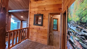 Un interior de madera con una escalera de madera, un espejo y un cuadro que muestra un arroyo rocoso.