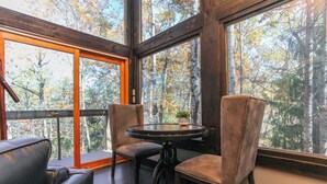 A cozy seating area with a round table and two chairs, large windows offering a view of a forested area. - Woodland Loft 1 - Modern-Industrial Mountain Getaway for Two (Bryson City)