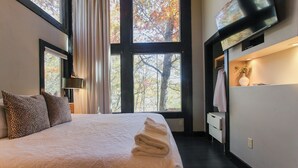 Ein Hotelzimmer mit einem großen Bett, einem an der Wand montierten Fernseher und einem Fenster mit Blick auf Bäume.