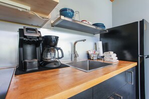 A kitchenette with a coffee maker, a kettle, a sink, and a refrigerator.