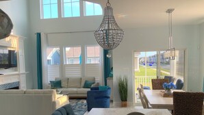 A spacious living room with a large window, a sofa, a dining table, and a kitchen area.