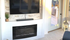 A modern living room with a flat-screen TV mounted on a stone wall, a fireplace below, and a door leading outside.