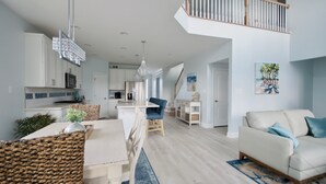 A spacious living area with a high ceiling, a dining table, a sofa, and a kitchen in the background.