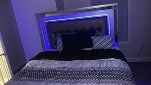 A bedroom with a tufted headboard, a bed with patterned bedding, and a window with blinds.