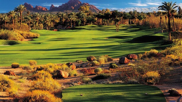 Un campo de golf con paisaje desértico, palmeras y montañas al fondo.