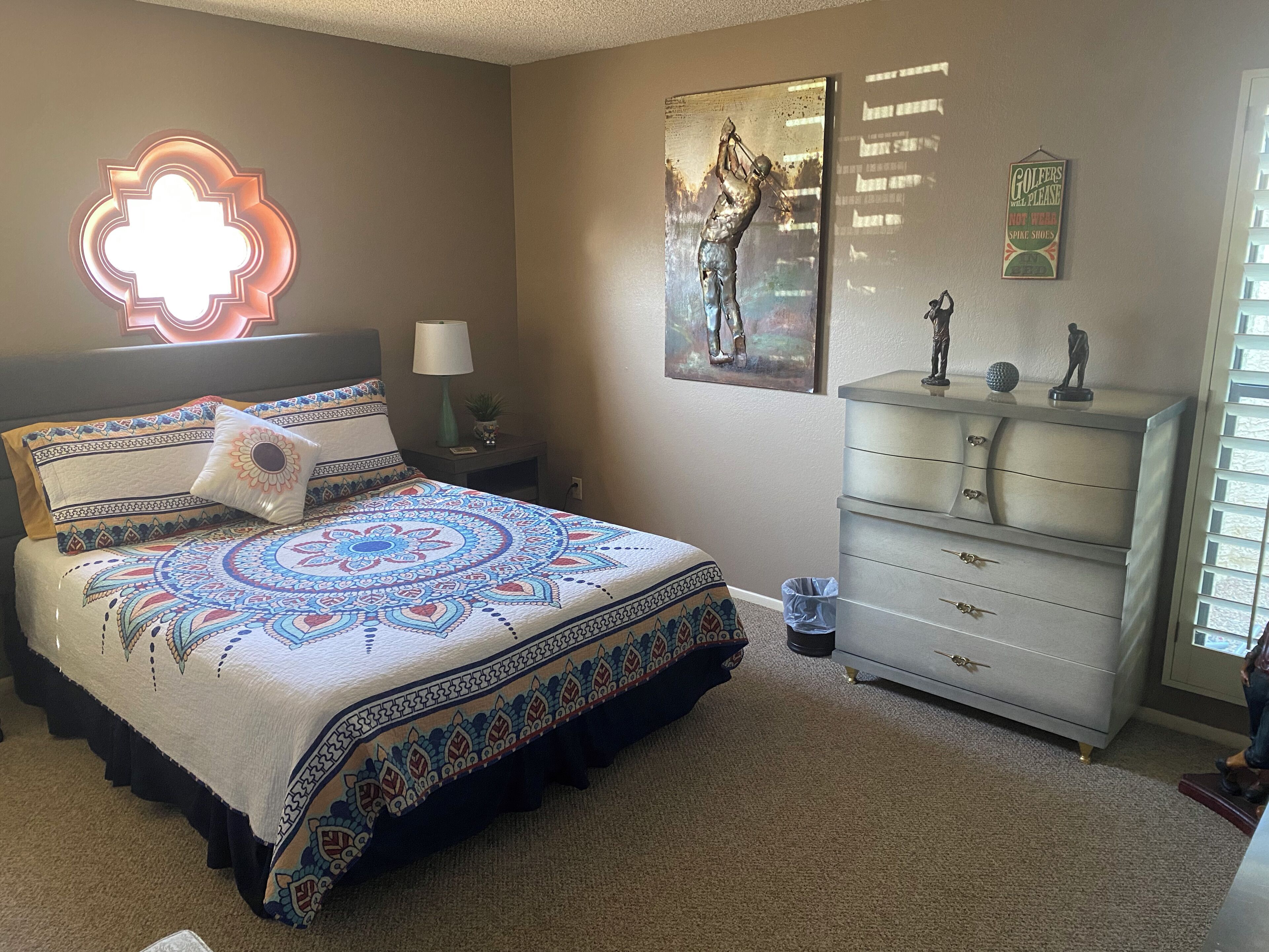 A bedroom with a bed, a dresser, a nightstand, a wall-mounted lamp, and a decorative wall piece.