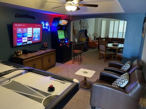 A room with a pool table, a television displaying streaming services, and a gaming console.