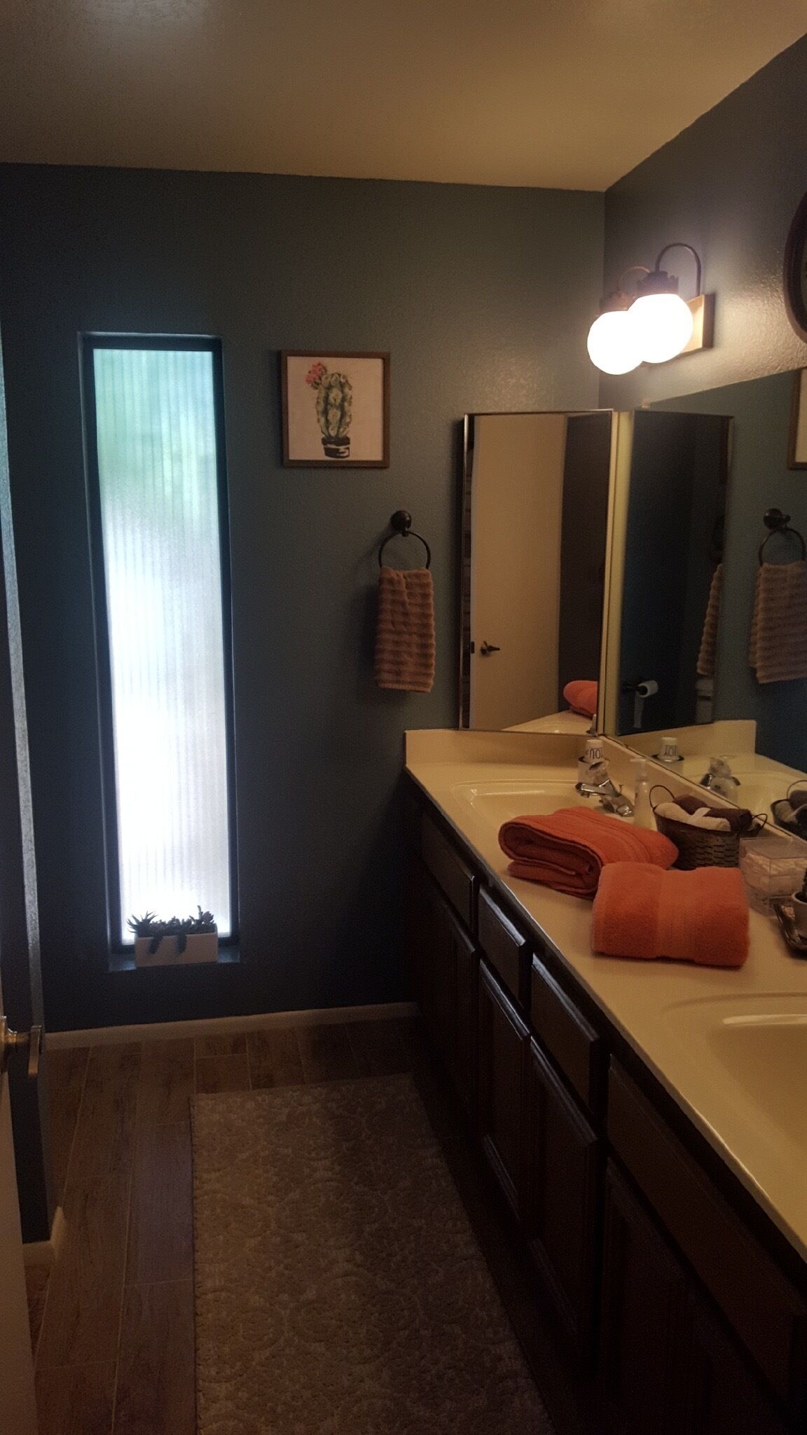 A bathroom with a large window, a sink with a mirror, and a towel rack.