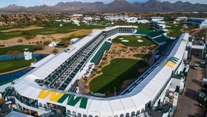 Un campo de golf con un amplio club de campo, varias áreas de práctica y montañas al fondo.