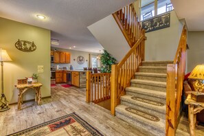 Ein geräumiger Wohnbereich mit einer Holztreppe, einer Küche im Hintergrund und einem dekorativen Wandschild.