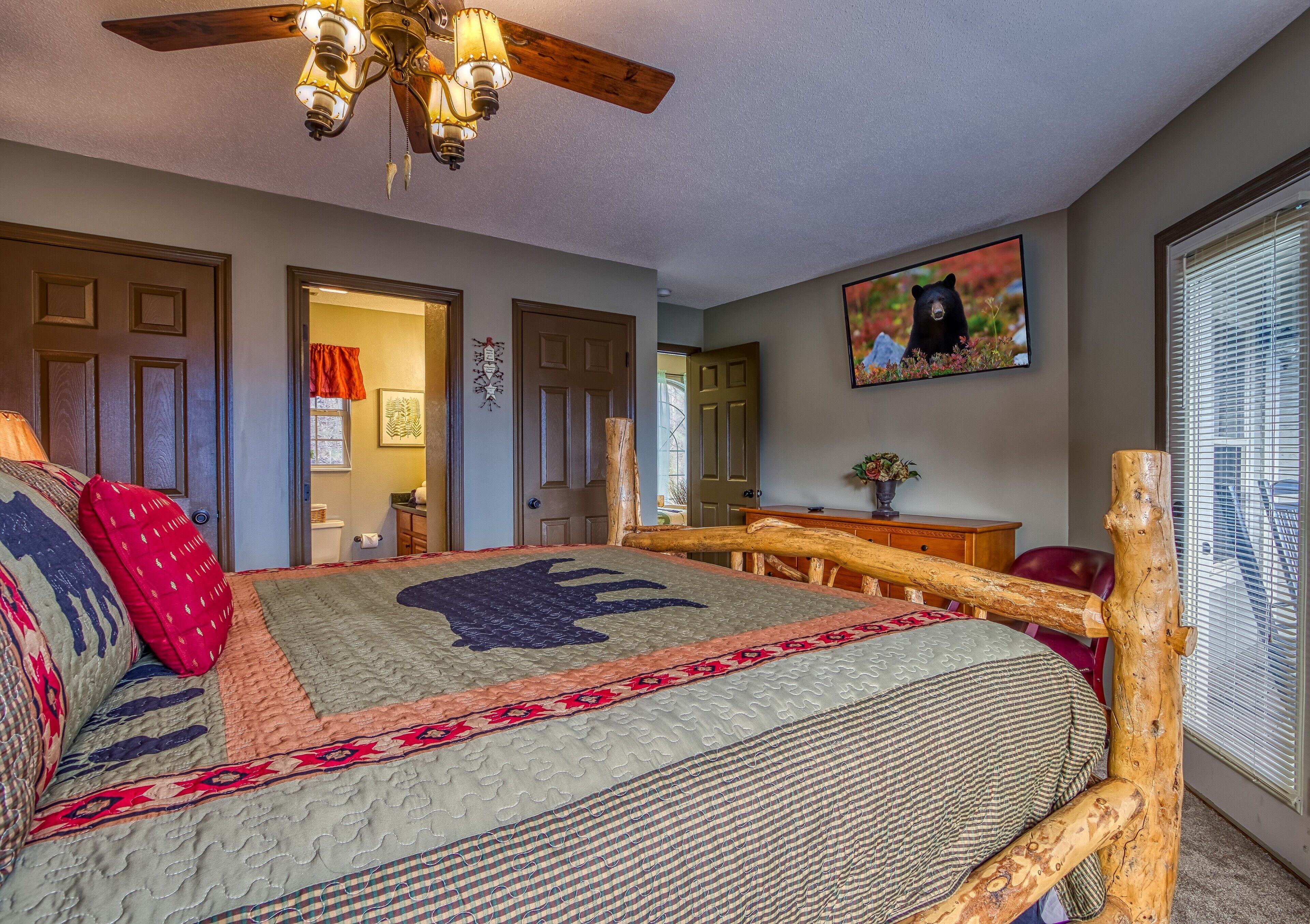 Un dormitorio con una cama grande, cabecera de madera, ventilador de techo, televisor y ventana con persianas.