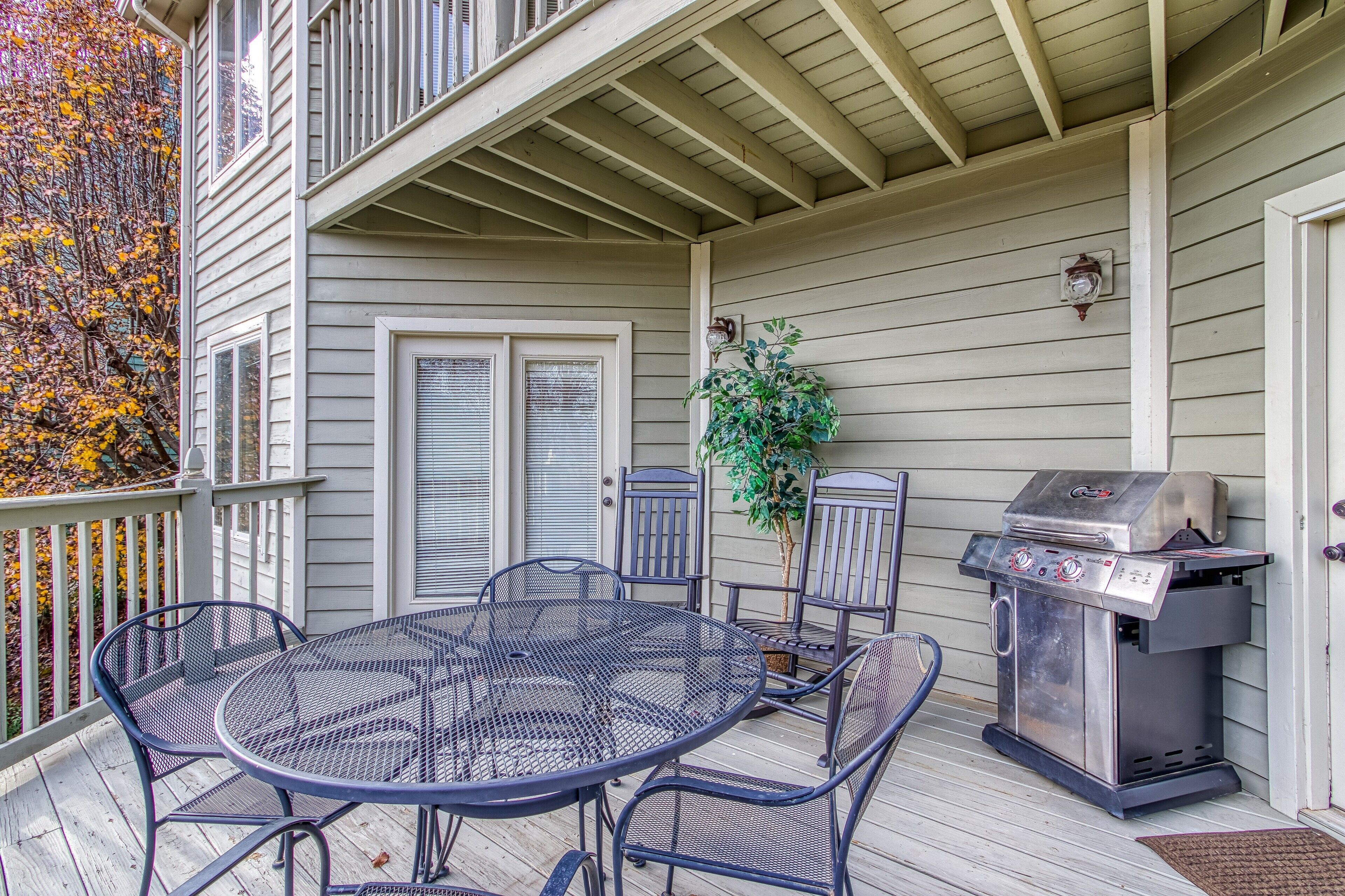 A covered patio with a metal table and chairs, a grill, and a potted plant.