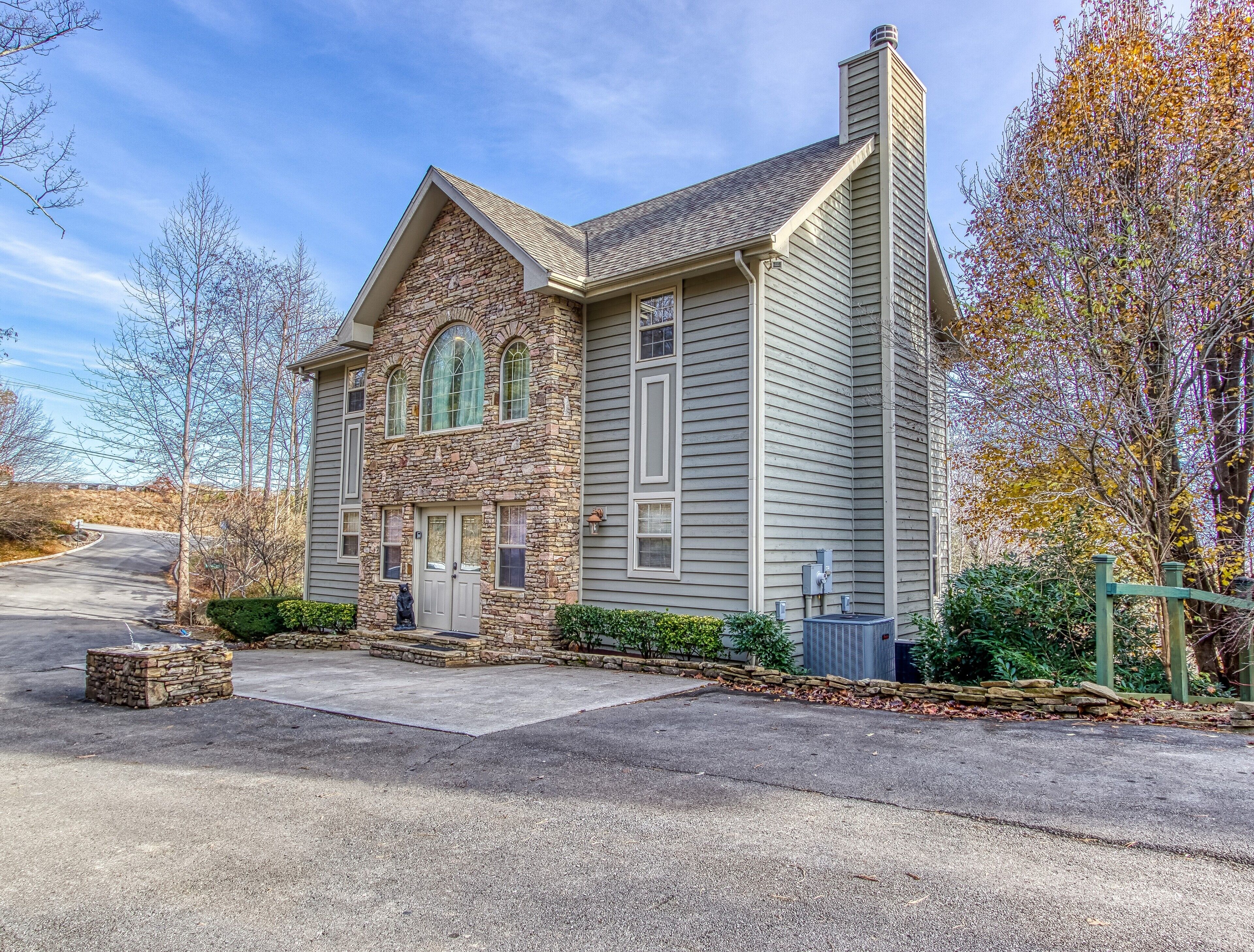 A two-story stone and siding house with a stone facade, a large arched window, and a chimney.