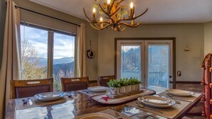 A dining area with a large table set for four, a chandelier, and a view of mountains through the windows.
